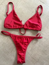Conjunto de bikini rojo brillante, compuesto por un corpiño triangular con tirantes finos y una tanga con tirantes laterales ajustables.
