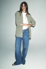 Blazer color blanco, abierta, con cuello solapa y hombreras. Manga tres cuartos acabada en vuelta con trabilla y botón dorado. Bolsillos delanteros con solapa.
