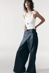 Pantalón de tiro medio azul denim, con trabillas en la cintura y cinturón ajustable con botones. Tiene bolsillos laterales ocultos y pierna ancha.