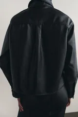 Sobrecamisa negra de efecto piel, con cuello de solapa, manga larga con puños abotonados, bajo recto y cierre frontal con botones.