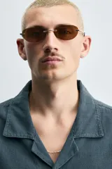 Camisa de denim de algodón, color beige claro, con corte relajado, cuello bowling y manga corta. Presenta cierre frontal con botones a presión y un pequeño bordado a tono en el pecho.