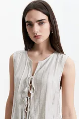 Blusa sin mangas color beige con lazo frontal y textura liviana.