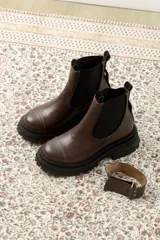 Botas de cuero color marrón oscuro, estilo Chelsea, con elástico lateral negro y suela track negra. Incluye correa de cuero desmontable con hebilla.