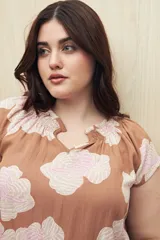 Blusa color marrón con estampado floral en tonos blanco y rosa, de corte holgado y mangas cortas.