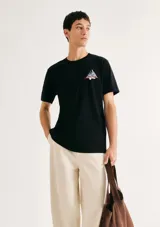 Camiseta blanca de algodón con cuello redondo y mangas cortas. Estampa rectangular con borde negro que contiene la frase "NATURAL ATMOSPHERE" en letras mayúsculas y una imagen de montañas y mar.