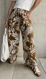 Pantalón marrón con estampado de hojas y flores blancas, de corte holgado y cintura elástica con lazo.