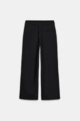 Pantalón negro con finas rayas verticales blancas, de tiro medio y corte ancho. Presenta bolsillos delanteros y traseros, cintura doble tipo bóxer con botones y cierre frontal con cremallera y ganchos metálicos. Detalle de franja marrón en los laterales.