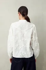 Camisa blanca con bordado floral en contraste, cuello mao, abotonadura frontal y mangas largas con frunces en los hombros.