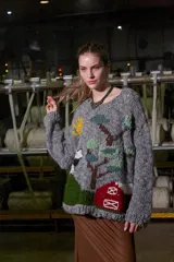 Sweater tejido de lana color gris con cuello redondo y puños acanalados. Presenta un diseño bordado a mano con motivos campestres: sol, vaca, árbol y granero.
