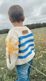 Sweater tejido de lana merino color crudo, con rayas horizontales azules y detalle de sol amarillo en una manga.
