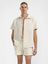 Short de baño color beige con una franja vertical marrón en el lateral. Tiene cintura elástica con cordón ajustable, bolsillos laterales y trasero con cierre, y suspensor de malla fina hipoalergénica.