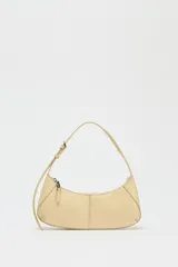 Bolso de hombro color crema, con forma alargada y asa ajustable con hebilla. Tiene pespuntes en el cuerpo, bolsillo interior con cremallera y cierre principal con cremallera y tirador.