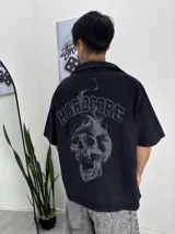 Camisa de manga corta negra con lavado oscuro, corte boxyfit, cuello camisero y estampado grande en la espalda de una calavera con llamas y el texto "HARDCORE" arriba.