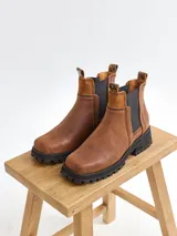 Botas de cuero marrón oscuro de alta calidad, con acabado mate y textura de gamuza, diseño por encima del tobillo y elástico lateral.