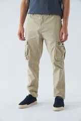 Pantalón cargo color beige, corte slim, con cierre y botón en la cintura, pasacintos, bolsillos cargo con botones y sin puños.