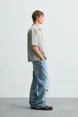 Camisa de hombre de corte boxy fit, confeccionada en tejido de algodón a cuadros en tonos beige, verde y azul. Tiene cuello solapa, manga corta y cierre frontal con botones.