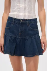 Minifalda de jean azul medio con diseño acampanado y detalle de volado en el ruedo. Cuenta con cierre frontal de botón y cremallera, y bolsillos laterales.