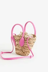 Cartera bandolera de paja color beige, con forro de tela color crema con cierre de cordón ajustable. Tiene dos asas cortas y correa larga ajustable de color rosa.