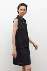 Vestido negro sin mangas con cuello camisero y cierre frontal con cordones. Presenta dos bolsillos con solapa a la altura del pecho y dos bolsillos laterales a la altura de la cadera.