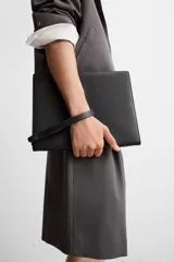 Bolso tipo sobre negro de cuero, con costura central y asa de mano. Cierre con cremallera y compartimentos interiores.