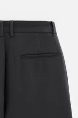 Pantalón relaxed fit color verde oscuro, con pliegues en la parte delantera, bolsillos laterales y traseros de ojal. Cierre frontal con cremallera y botón.
