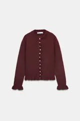 Cárdigan color borgoña de tejido de punto con cuello redondo y manga larga. Presenta volantes en los puños y en el borde inferior, y cierre frontal con botones blancos.
