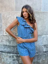 Mono corto azul con estampado de flores blancas, un hombro descubierto con volantes y cintura elástica.