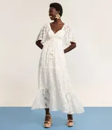 Vestido largo evasé de crepé blanco con textura y volados. Tiene escote corazón, elástico en la cintura, lazo con cordón y borla en las puntas, y mangas cortas.