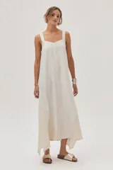 Vestido largo color crema, con breteles anchos y escote recto. Presenta corte irregular en el ruedo y volado en el bajo.