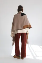 Ruana tejida con diseño geométrico en bloques de color beige, azul y naranja, con flecos en el borde inferior.