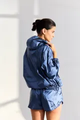 Campera azul de tejido rompevientos con efecto satinado, calce holgado, capucha, cintura ajustable y bolsillos frontales.