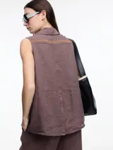 Camisa sin mangas negra de lino con cuello clásico, cierre frontal abotonado y bolsillo de parche en el pecho. Presenta bordados tipo pespunte en contraste en el frente y canesú trasero.