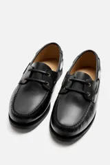 Zapato náutico de cuero negro con cordones de cuero y suela plana.