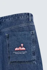 Pantalón de jean azul oscuro, corte tapered wide fit, tiro medio, cinco bolsillos, detalle de texto bordado en trasero, efecto lavado y cierre frontal con cremallera y botón.