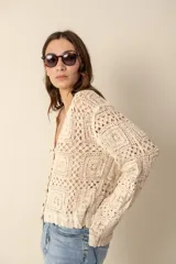 Cardigan color crema tejido al crochet con diseño calado, escote en V y cierre frontal con botones.