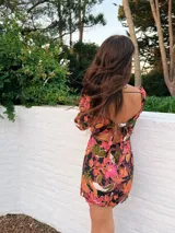 Minivestido marrón con estampado floral en tonos naranja, rosa y verde. Tiene escote cuadrado con abertura en el centro, mangas largas y falda con tajo lateral.