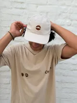 Gorro tipo gorra de béisbol color crudo con visera curva y logo bordado en el centro.