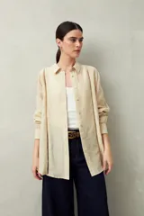 Camisa blanca de lino con botones de nácar, corte recto, cuello clásico y mangas largas con puños abotonados. Presenta detalles de calados tipo vainillas en el frente y las mangas.