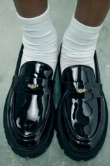 Zapato tipo mocasín negro acharolado con antifaz y suela track.