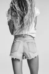 Short de jean de tiro alto, color celeste claro desgastado, con roturas grandes y deshilachado en el bajo. Presenta cinco bolsillos y cierre frontal con botón metálico.