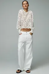 Top de encaje blanco con cuello redondo, mangas largas abullonadas y puños con botones metálicos.
