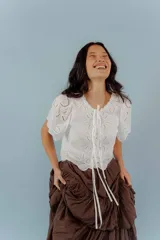 Blusa negra con bordado calado, escote en V con lazos para atar y mangas cortas abullonadas.