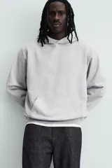 Sudadera con capucha color crudo, de corte relajado, confeccionada en tejido de algodón con interior rizado. Cuenta con cuello con capucha, manga larga, bolsillo frontal tipo canguro y acabados en rib.