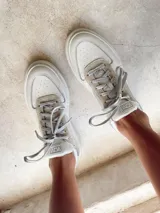 Championes blancos de cuero sintético con detalles en gamuza gris en la puntera y el talón. Cordones grises y suela de goma blanca.