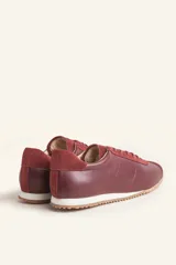 Zapatillas deportivas de cuero color borgoña con detalles en gamuza al tono, cordones finos y suela de goma blanca.