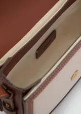 Bandolera rectangular color crudo con detalles en cuero marrón. Tiene correa larga ajustable, cierre con solapa y botón magnético, bolsillo interior y forro de algodón.