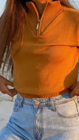 Polera de hilo color naranja con cierre en el cuello y ajuste en la cintura.