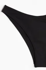 Parte inferior de bikini color negro, tiro bajo, con cintura curva y cobertura media en la parte trasera.