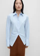 Camisa celeste de popelina de algodón y lyocell, de corte oversize, manga larga con puños abotonados, cuello camisero y cierre frontal con botones.