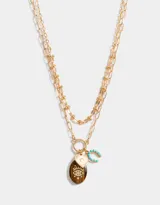 Collar corto dorado multicadena con eslabones de distintos grosores y dijes místicos con piedra ojo de tigre, corazón y letra C con strass.